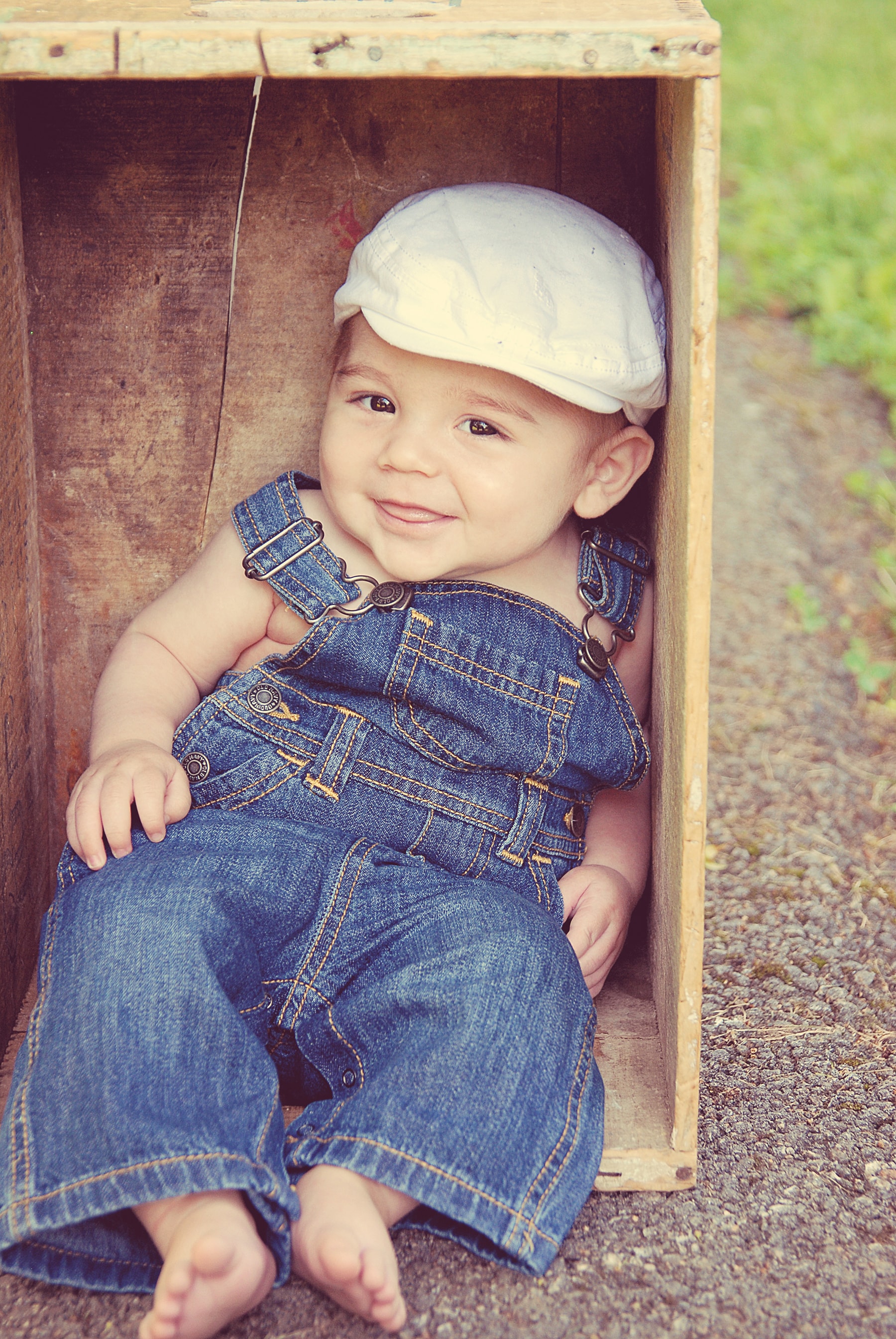 Toddler in overalls sitting in wooden box