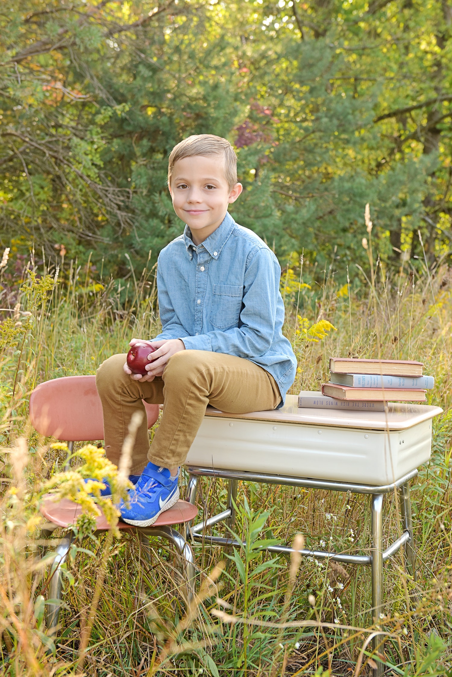 Boy sitting outdoors with books and apple